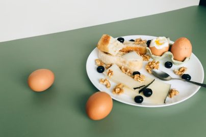 Plate of cheese, boiled eggs, bread, walnuts, and blueberries for a hearty breakfast.