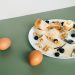 Plate of cheese, boiled eggs, bread, walnuts, and blueberries for a hearty breakfast.